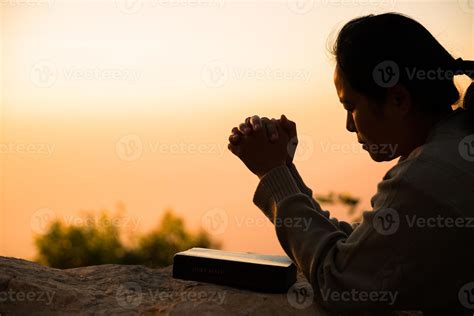 Silhouette of woman kneeling down praying for worship God at sky background. Christians pray to ...