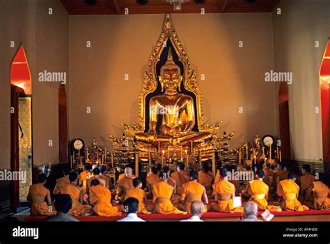 Buddhist Temple interior with lines of the backs of monks at worship looking towards statue of ...