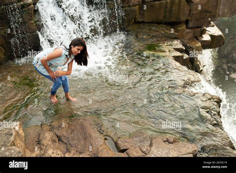 Attractive young Indian woman wearing jeans and smiling while playing with water surrounded by ...