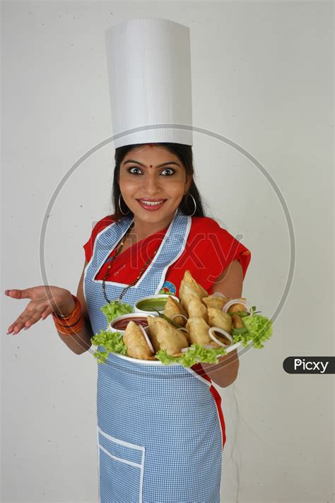 Image of An Indian Woman Chef In Kitchen Apron And Cap Holding Samosas Plate With an Expression ...
