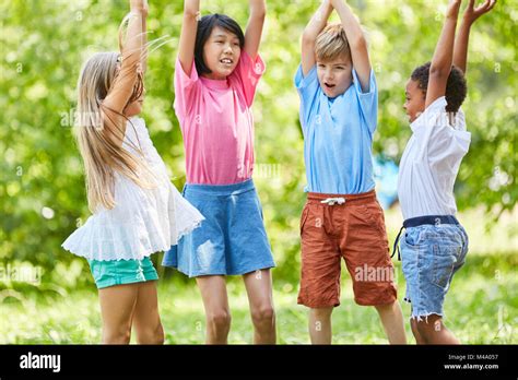 Group of kids as friends play together in the park and raise hands Stock Photo - Alamy