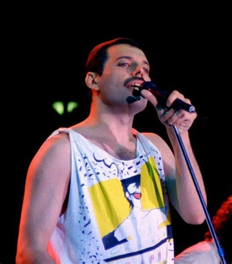 a man standing on stage with a microphone in his hand and wearing a ...