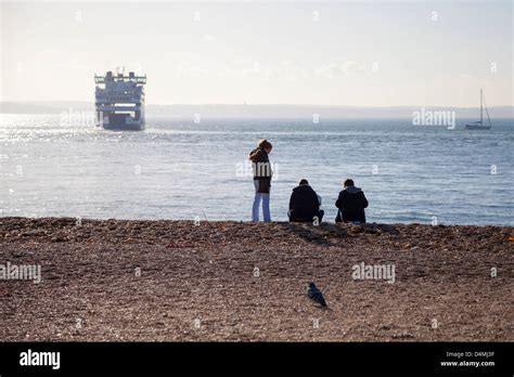 People on Southsea Beach in Portsmouth looking out to a Wightlink car ferry in the Solent ...