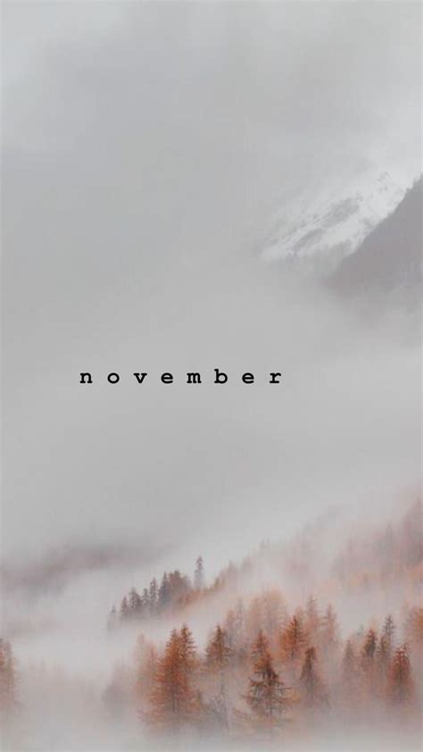 the words november are surrounded by fog and trees in front of a mountain range with low lying ...