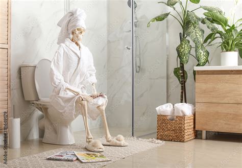 Skeleton in bathrobe with mobile phone sitting on toilet bowl Stock Photo | Adobe Stock