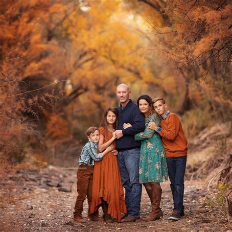 a family posing for a photo in the woods with fall foliage behind them and trees turning orange