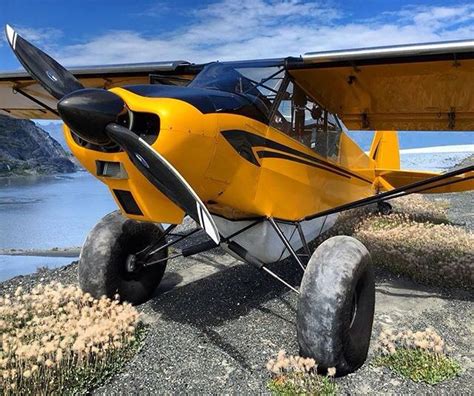 a yellow airplane parked on top of a field next to a body of water with ...