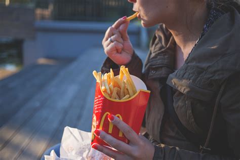 Woman in Brown Classic Trench Coat Eating Mcdo Fries during Daytime · Free Stock Photo