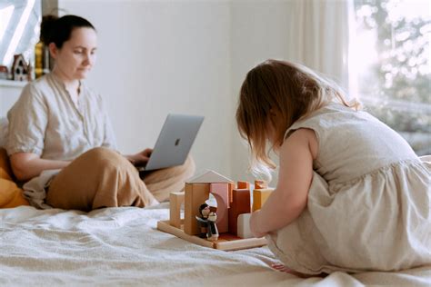 Cute toddler girl playing with wooden toys on bed while mother using laptop · Free Stock Photo