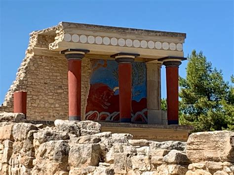 an ancient building with red columns and paintings on the side, in front of some trees