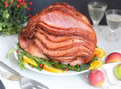 a large ham sitting on top of a white plate next to fruit and silverware