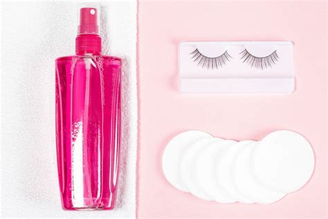 Makeup remover, white towel, cotton pads and false eyelashes on a pink background, top view ...