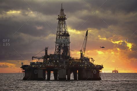 Oil rigs in sea against cloudy sky sunset stock photo - OFFSET