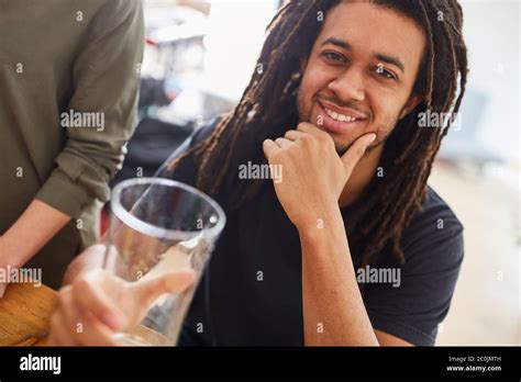 African man with dreadlocks sits smiling at the dining table with friends over a meal Stock ...