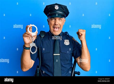 Handsome Middle Age Mature Man Wearing Police Uniform Holding Metal Handcuffs Screaming Proud