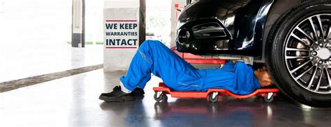 Mechanic In Blue Uniform Lying Down And Working Under Car At Aut