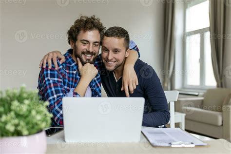 encantador gay Pareja riendo juntos mientras sentado en su vivo habitación a hogar dos