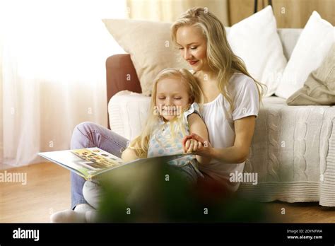 Bonne famille Une jeune mère blonde lit un livre à sa jolie fille tout en étant assise au sol