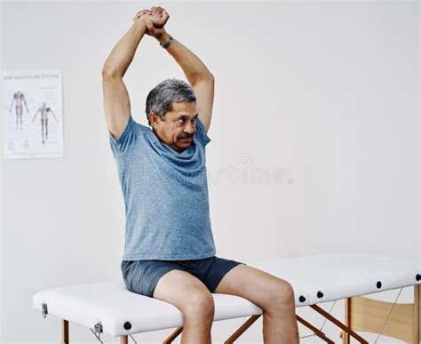 Stretching While He Waits For The Doctor A Handsome Mature Man Stretching While Sitting On A