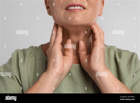 Mature Woman Doing Thyroid Self Examination On Light Grey Background