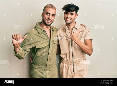 Homosexual Gay Couple Standing Together Wearing Casual Jumpsuit Pointing To The Back Behind With