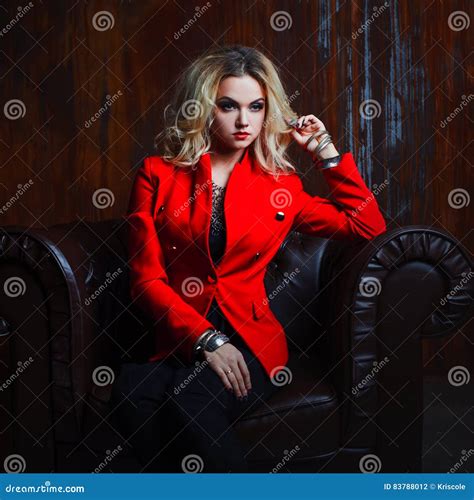Junge Und Attraktive Blonde Frau In Der Roten Jacke Sitzt Im Ledersessel Rostige Wand Des