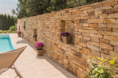 A Stone Wall Next To A Swimming Pool With Flowers In Pots On The Ledges