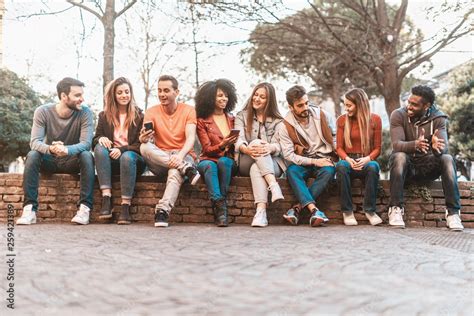 Group Of Multiracial Friends Disposed In A Row Sitting Outdoor Using