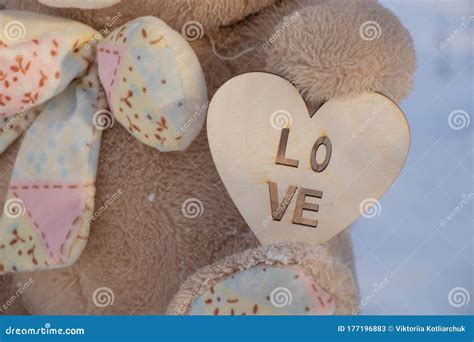 A Teddy Bear Holds A Wooden Heart In Its Paws On The Street In Winter