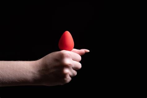 Tapón anal rojo en manos femeninas sobre un fondo negro aislado