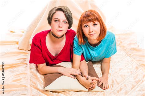 Two Lesbian Girls Lying On The Blanket Cover And Hold Hands On White