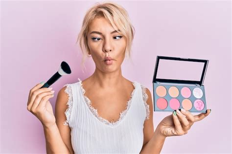 Jeune Fille Blonde Tenant Un Pinceau De Maquillage Et Rougissant Faisant Face Au Poisson Avec La