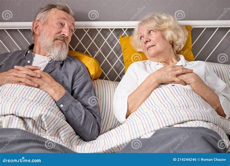 Two Lovely Senior Man And Woman Lie On Bed Together Looking At Each