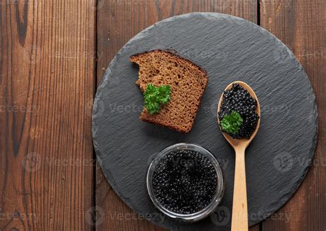 black paddlefish caviar in a wooden spoon, a slice of bread and a jar