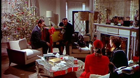 People Sitting Around In A Living Room With Christmas Decorations