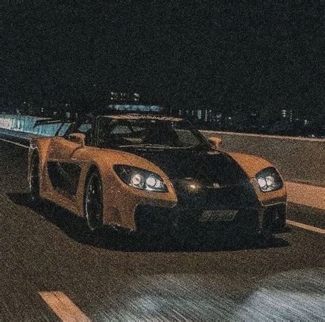 A Yellow Sports Car Driving Down The Road At Night