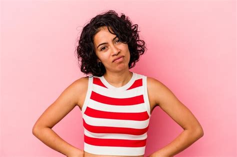 Joven mujer latina rizada aislada sobre fondo rosa cara triste seria sintiéndose miserable y