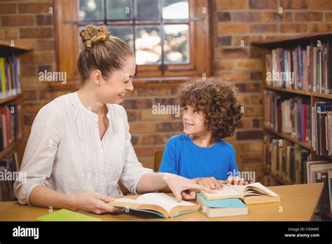 Blonde Teacher And Pupil Reading Books In The Library Stock Photo Alamy
