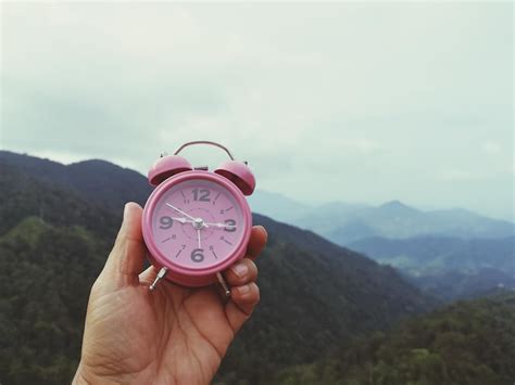 Premium Photo Cropped Hand Holding Alarm Clock Against Mountains