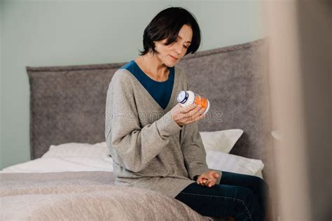 White Mature Woman Examining Medicine While Sitting On Bed Stock Photo Image Of Capsule