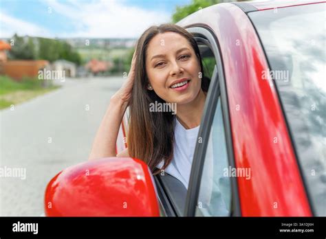 A Smiling Brunette Woman In A White Shirt Leans Out Of A Red Car Window Stock Photo Alamy