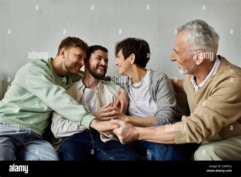 A Gay Couple Sits On A Couch With Parents Holding Hands And Smiling Warmly Stock Photo Alamy