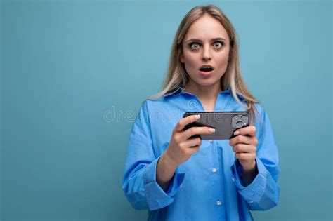 Puzzled Charming Blonde Girl Shocked Holding Smartphone In Hands Over Isolated Blue Background