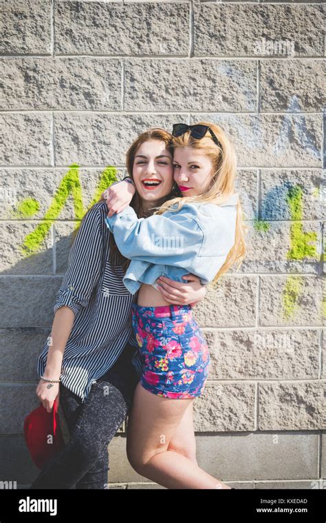 Two Beautiful Blonde And Brunette Girl Having Fun Posing On A Wall In The City Suburbs