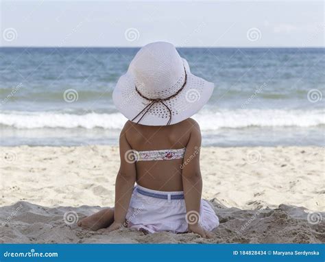 Petite Fille Dans Un Bikini Et Un Chapeau Blanc De Plage En Regardant La Mer Photo Stock Image