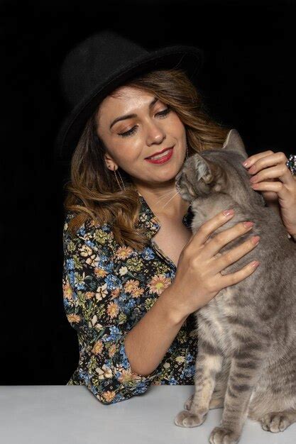 Joven Latina Con El Pelo Largo Y Un Sombrero Negro Acariciando A Su Gato De Fondo Negro Foto