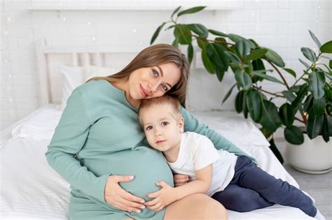 Bebe Barriguinha - Gestante e filho bebê toca uma barriguinha em casa na cama, conceito de ...