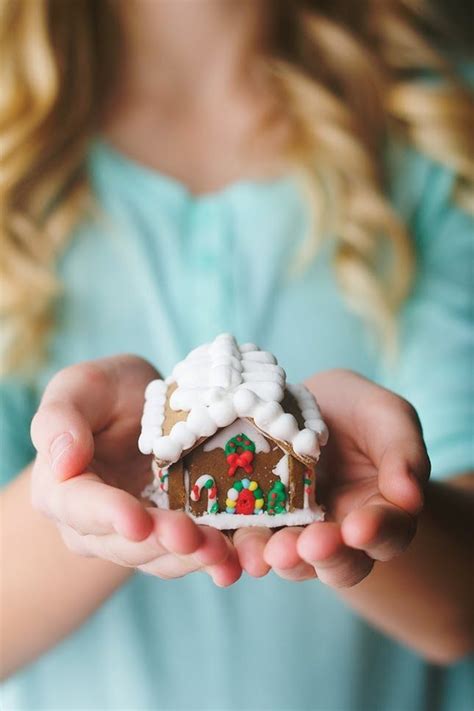 A Woman Holding A Small Gingerbread House In Her Hands With Snow On The