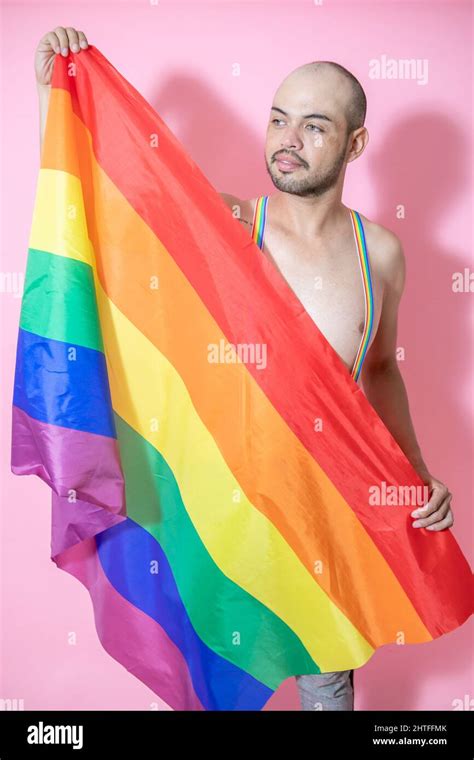 Un jeune homme chauve mexicain portant des bretelles de fierté gay posant avec le drapeau LGBT