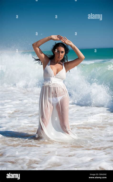 Beautiful Brunette Woman Wearing A White And Transparent Dress On The Water At The Beach Stock
